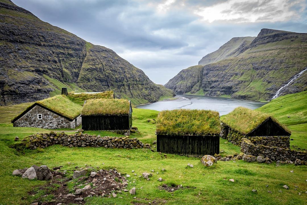 Turf-roof houses in the remote village of Saksun, Streymoy, Faroe Islands, with mountains and a tidal lagoon in the background.