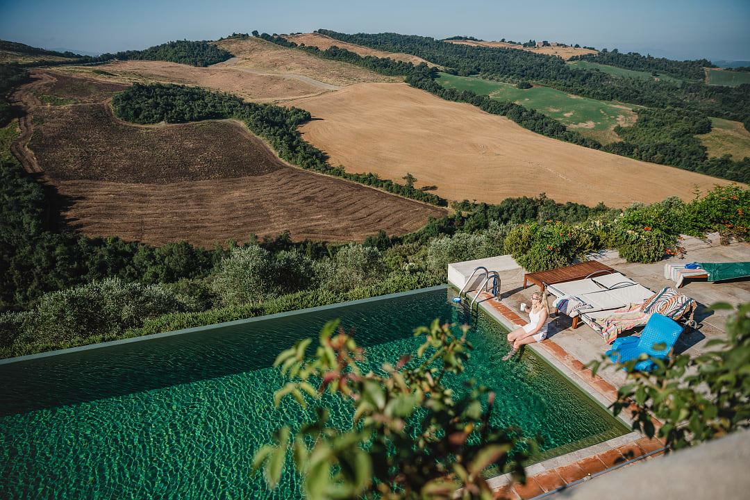 Woman Relaxing by a Pool Amidst the Patchwork Quilt of Silver-Green Tuscany Landscape.