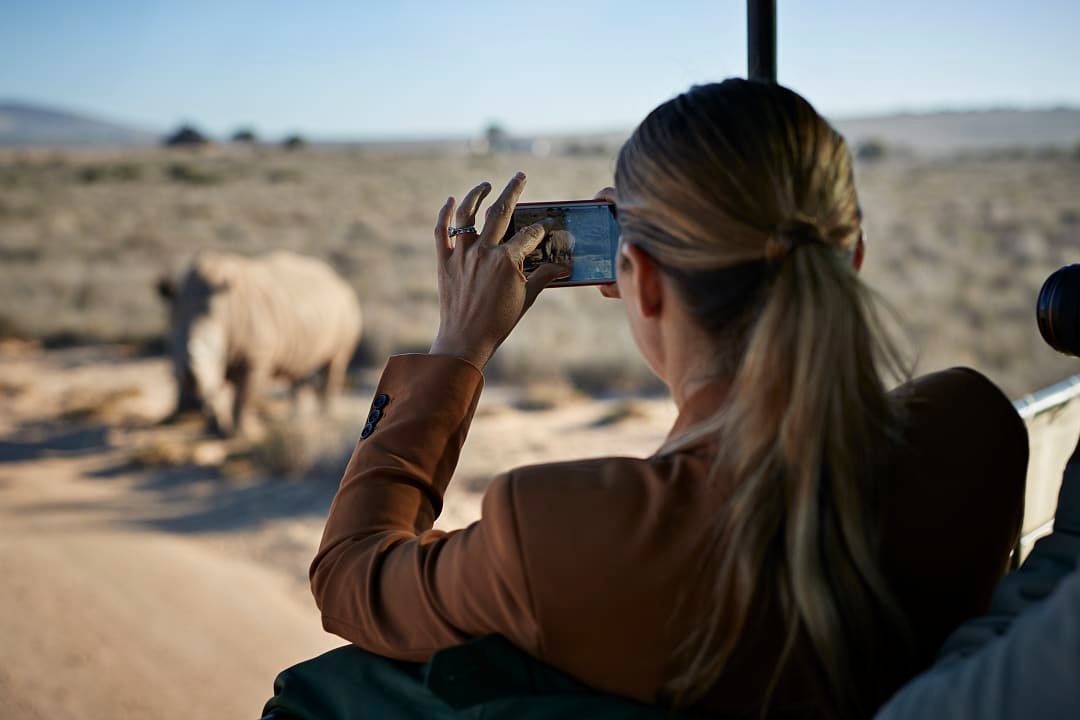 Woman on a safari game drive photographing a rhino with her mobile phone in South Africa