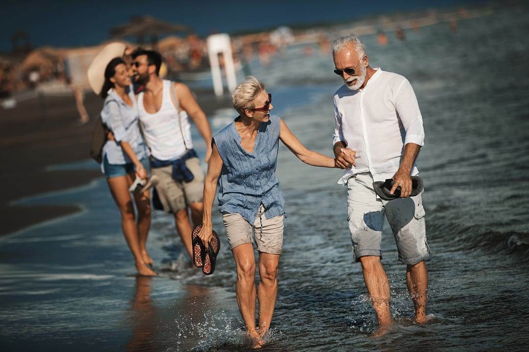 Multi-generational family walking along a sun-drenched beach in shallow water.