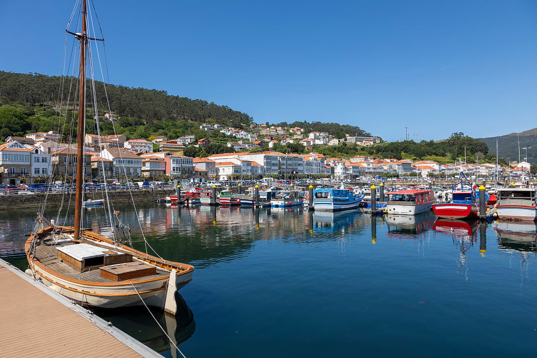 A quiet Galician harbor, featuring some fishing boats and white houses with tiled roofs.
