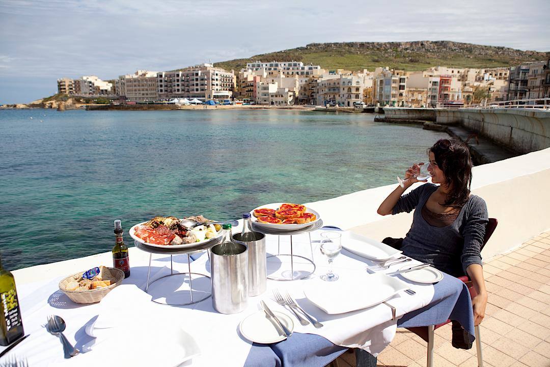 Woman enjoying a meal by the sea in Gozo, Malta.