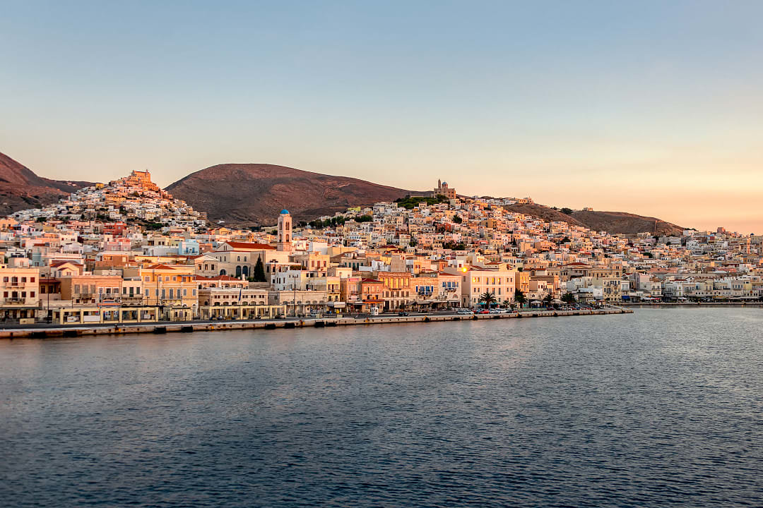 Sunset view of Ermoupoli’s neoclassical waterfront and hills on Syros Island, Greece