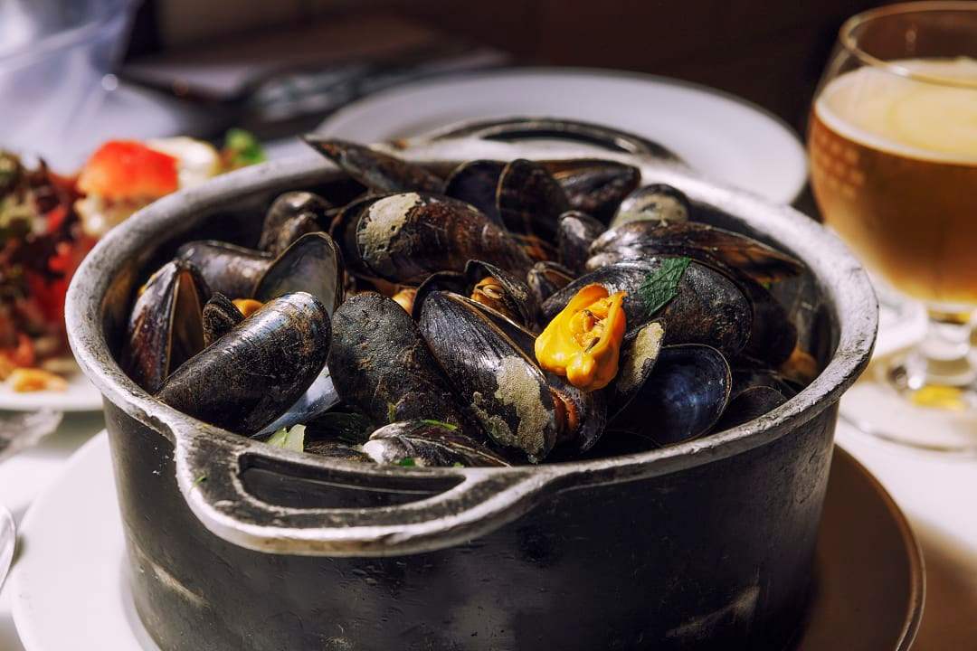 Steaming black pot filled with fresh mussels in broth.