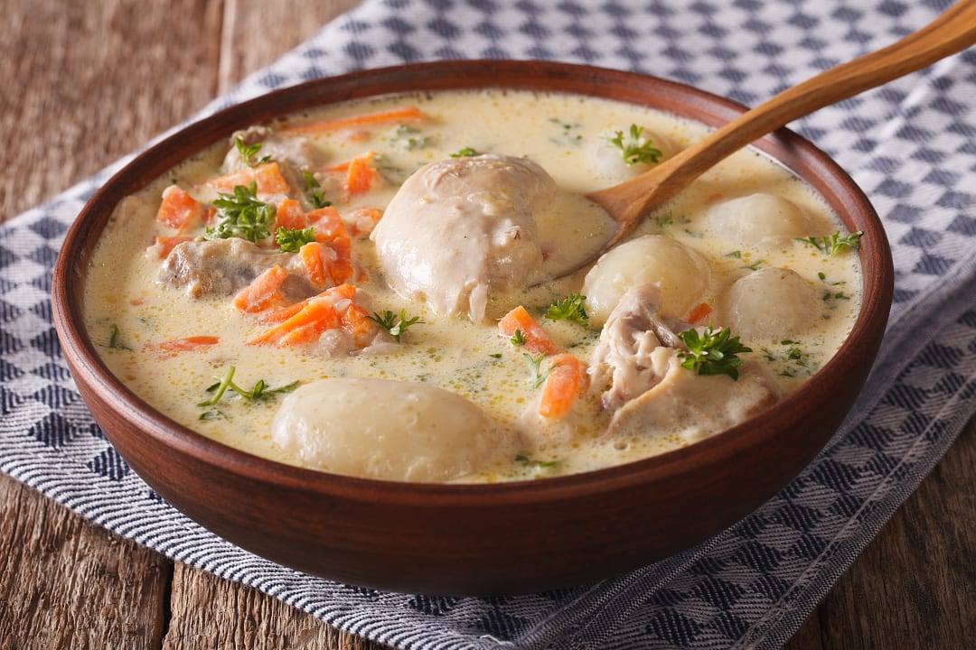 Ceramic bowl of creamy chicken stew with carrots and potatoes.