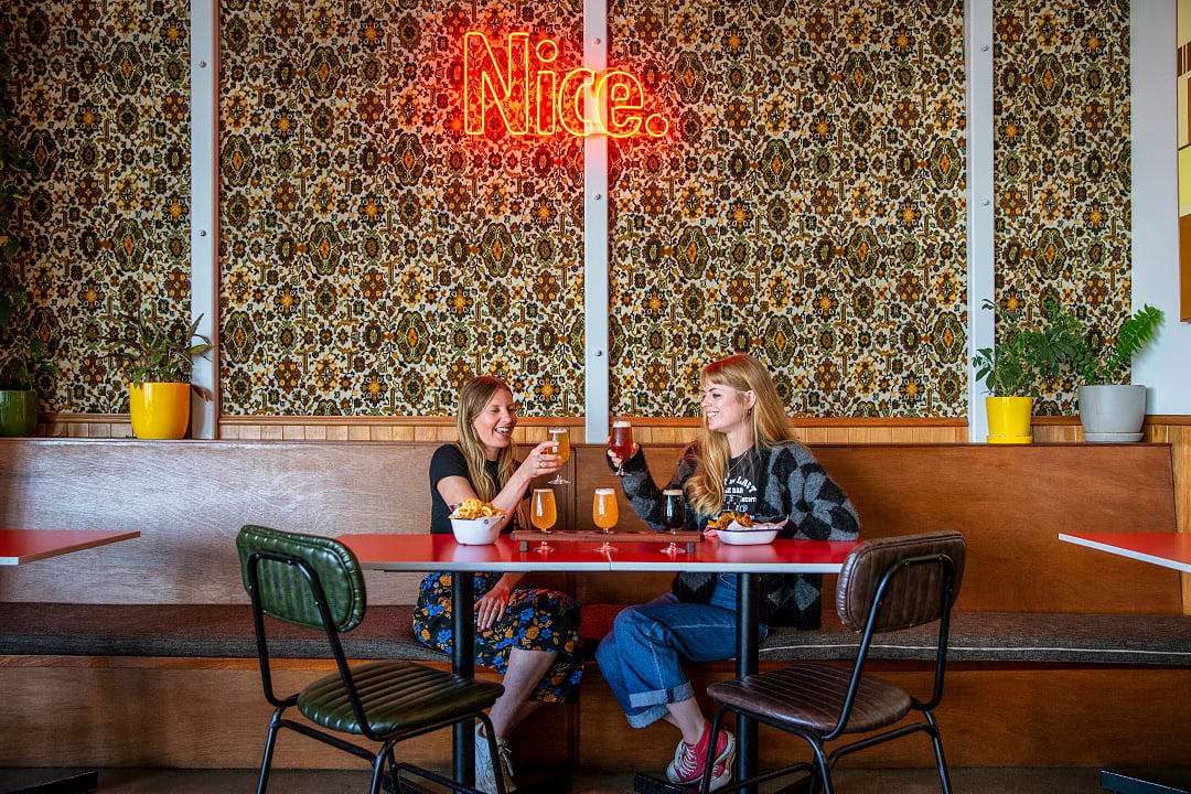 	Two women sitting at a retro-styled booth at Parrotdog Bar sampling beers from this Wellington brewery