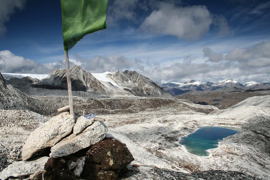 Flag posted in rocks flying from viewpoint at Rinchen Zoe La pass in Bhutan with scenic peaks, rocky valley with alpine lake