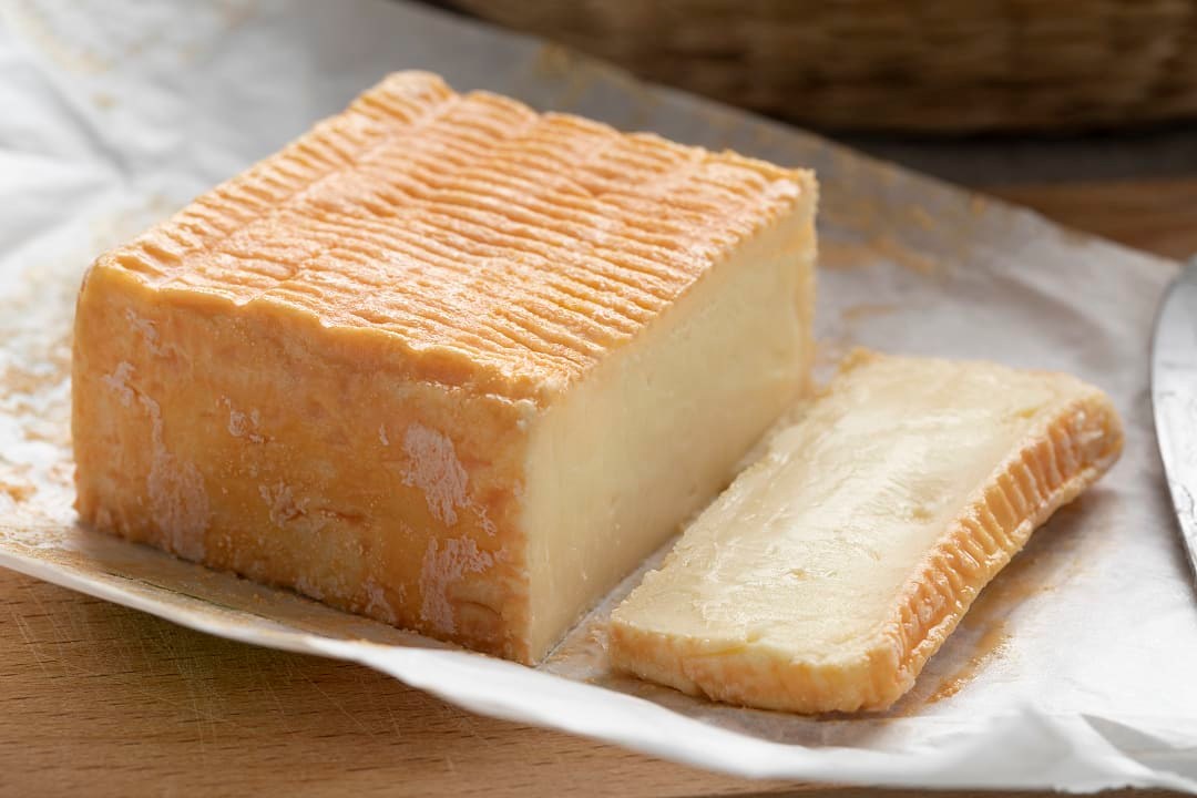 Close-up of a block of orange-rind Herve cheese with a sliced wedge.