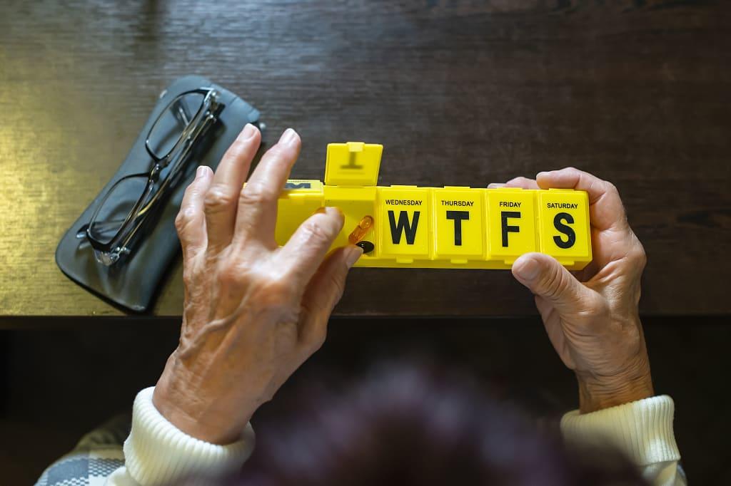 Senior woman removing mediation from yellow pill box
