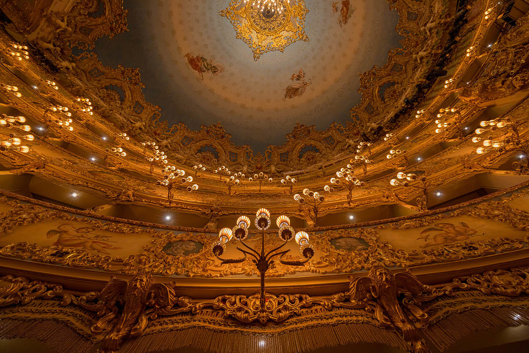 Ornate Teatro La Fenice opera house interior with golden balconies, chandeliers, and a beautifully painted ceiling