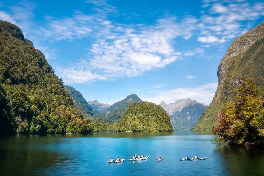 Kayakers paddle through tranquil Doubtful Sound fjord in Fiordland wilderness.