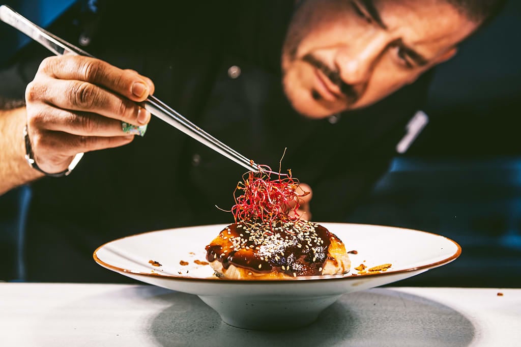 Chef garnishing a gourmet dish with tweezers in a fine dining restaurant kitchen