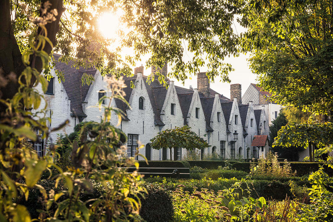 White gabled almshouses surrounded by gardens in the historic center of Bruges, Belgium.