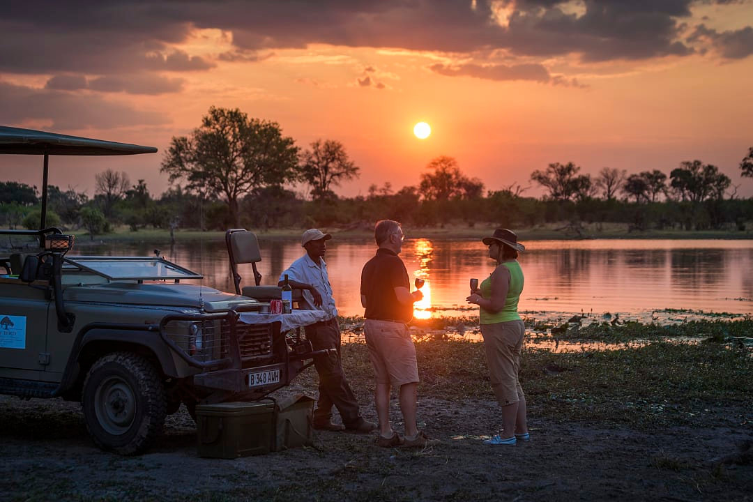 Senior travelers enjoying a sundowner with their private guide on the banks of the Khwai river in the Okavango Delta, Botswana