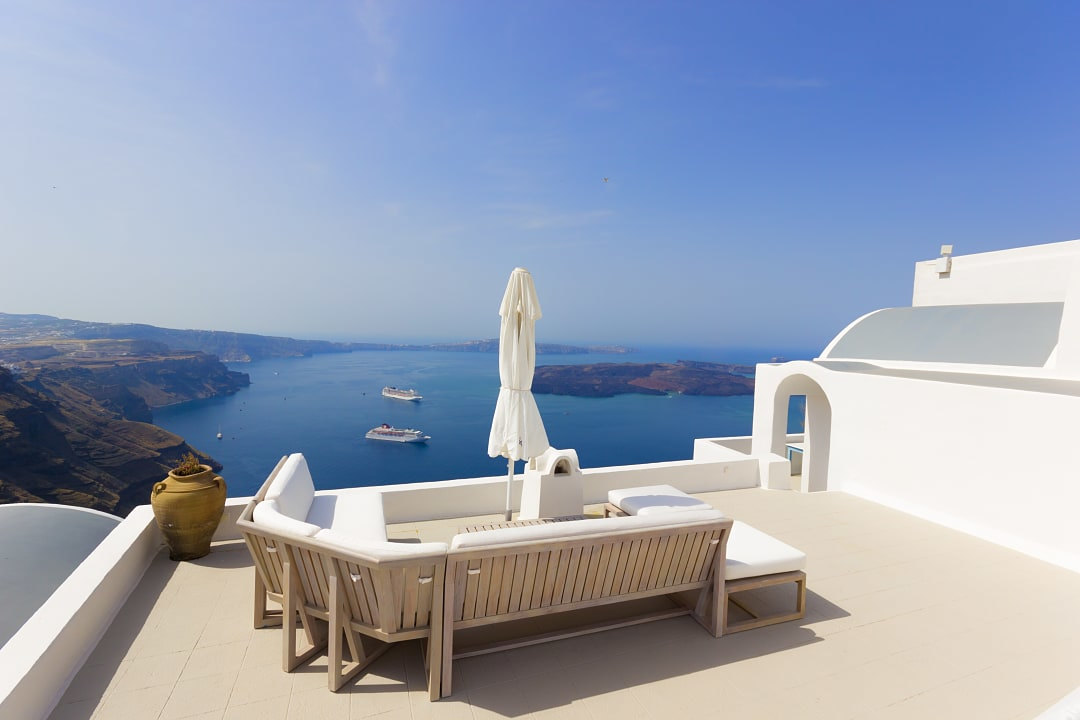 White patio with lounge furniture overlooking a deep blue sea.