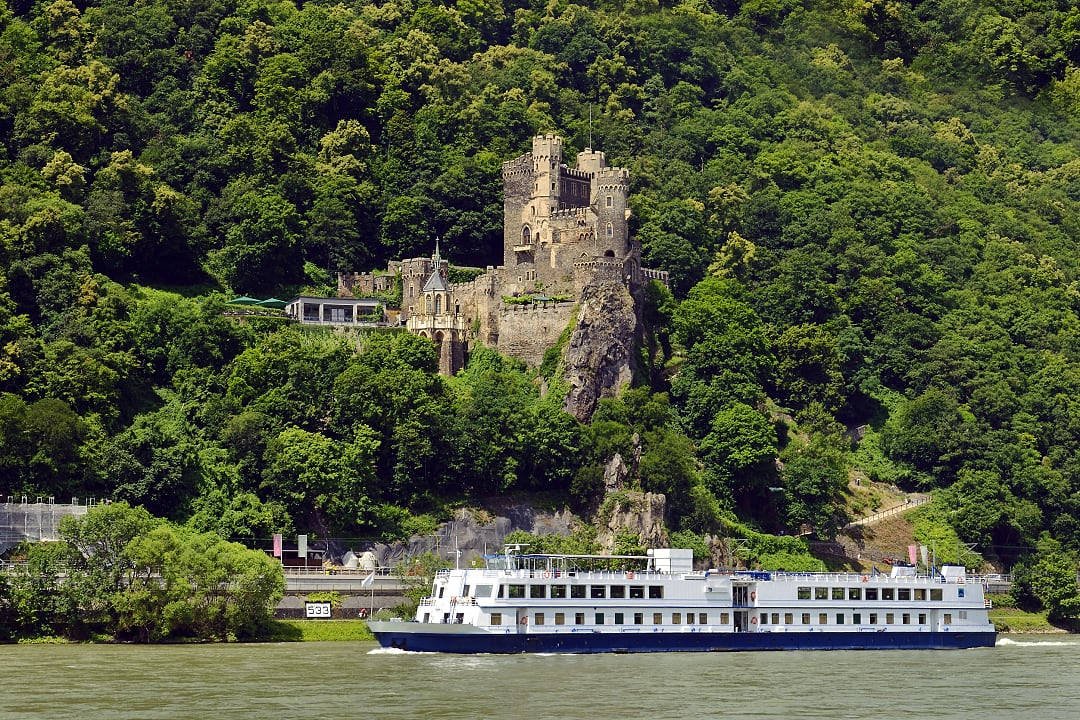 Cruise ship and Castle Rheinstein on a rocky cliff overlooking the Rhine River in Germany.