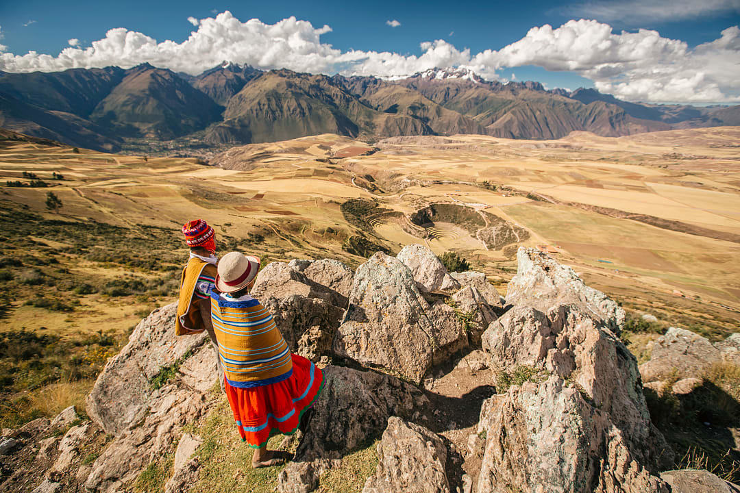 Two locals in traditional clothing overlooking the Sacred Valley and Moray terraces in Peru's Andes Mountains
