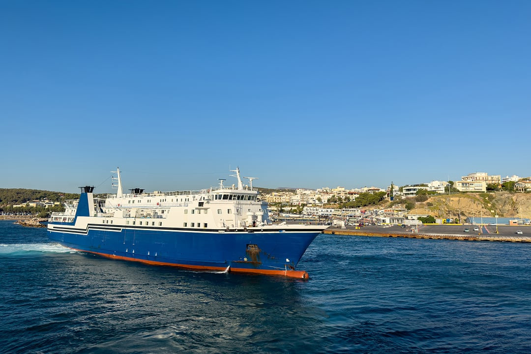 Large blue and white passenger ferry sailing near a coastline.