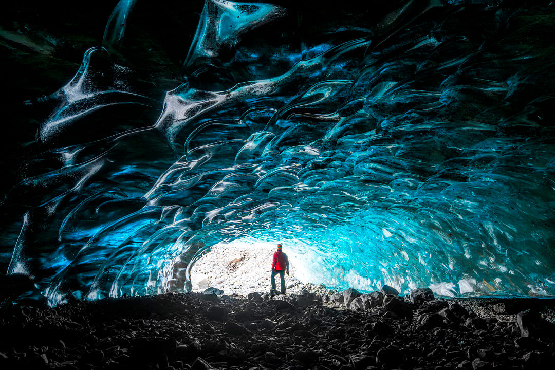 Person standing inside shimmering blue ice cave in Vatnajökull glacier.