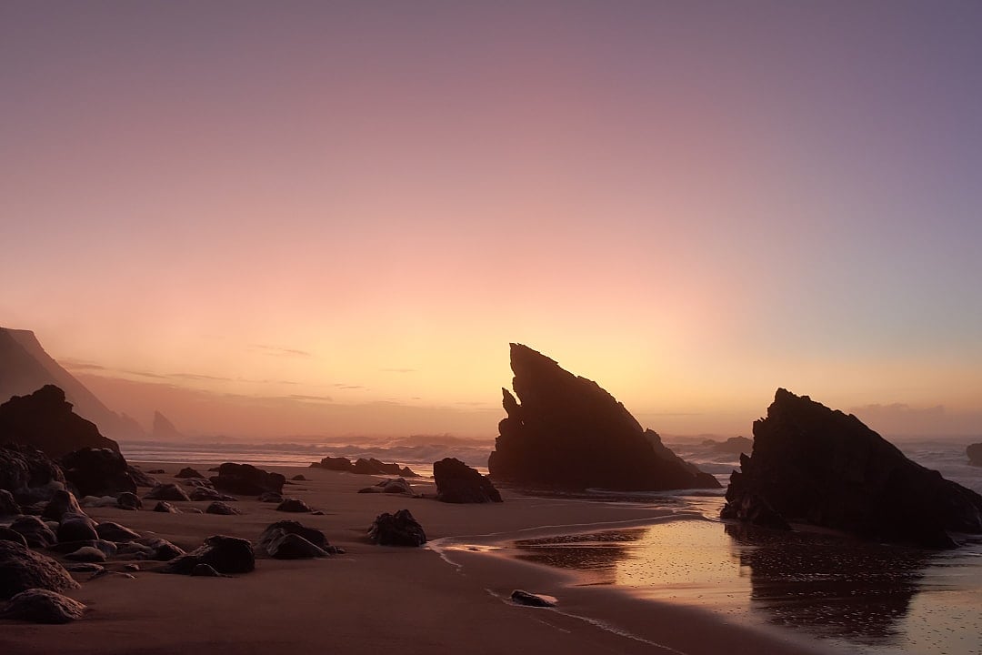 Rocks silhouetted against misty sunset over the Atlantic ocean on Praia da Adraga in Sintra