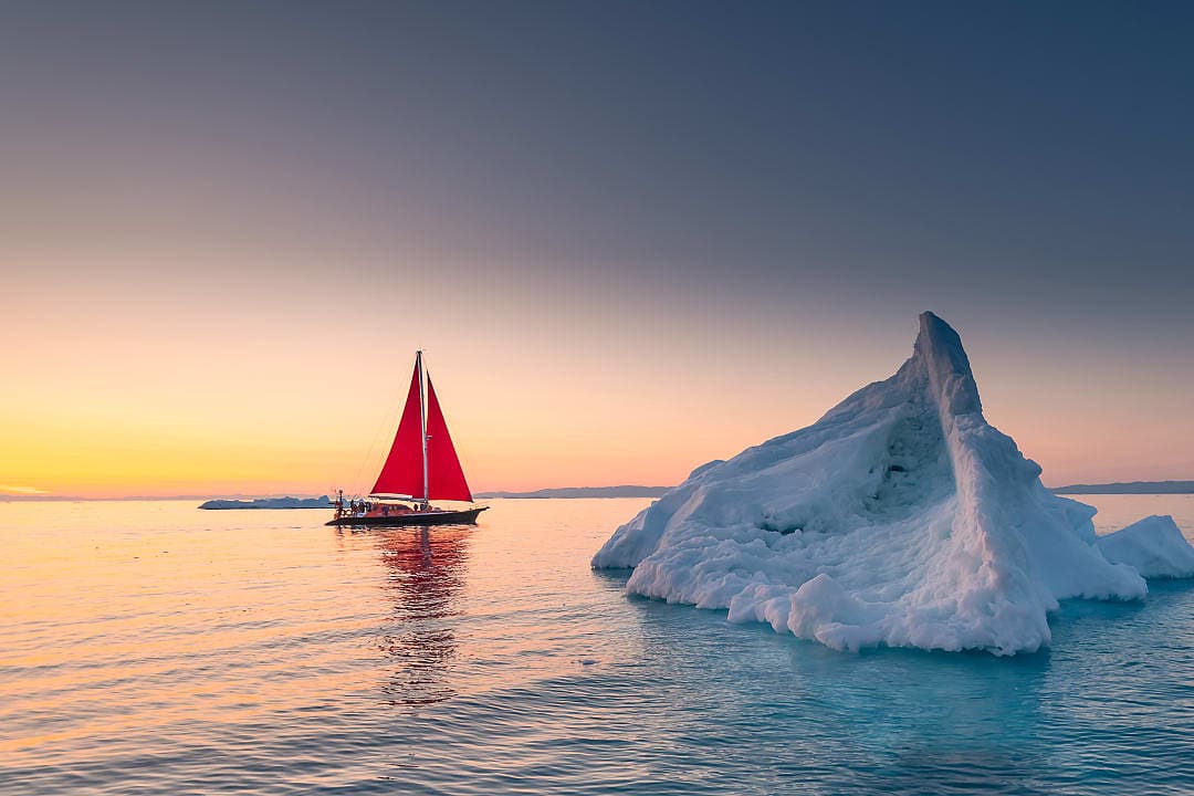 A sailing charter navigating the waters surrounding some icebergs in Greenland.