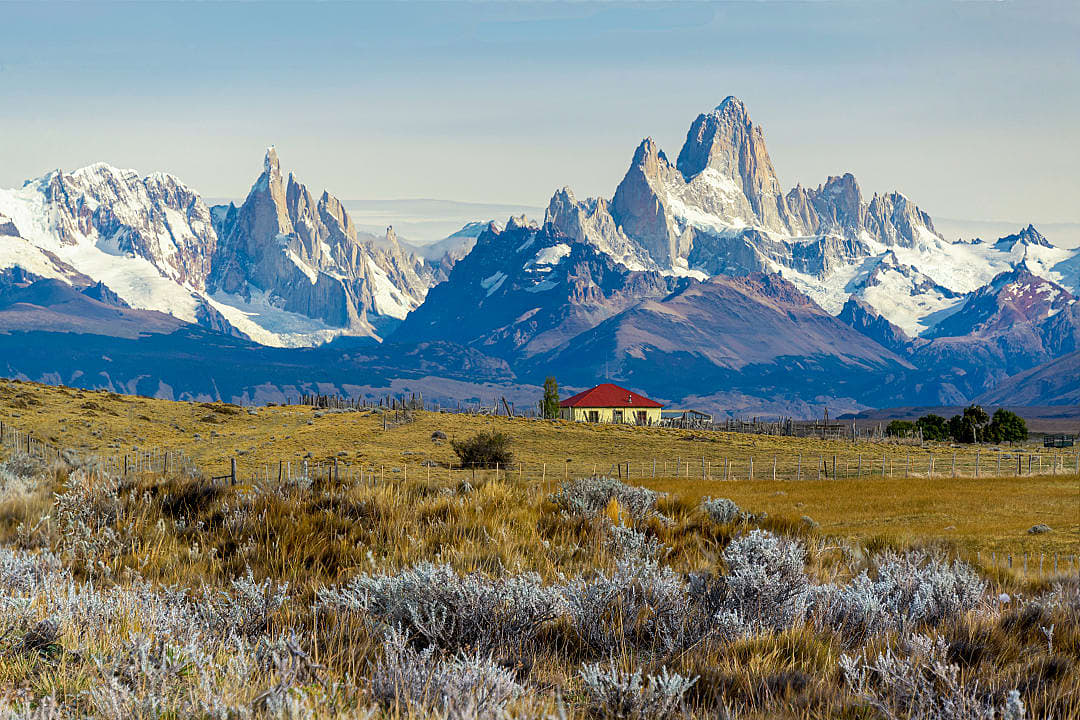 A remote estancia sits beneath towering, snow-capped mountains in Patagonia.