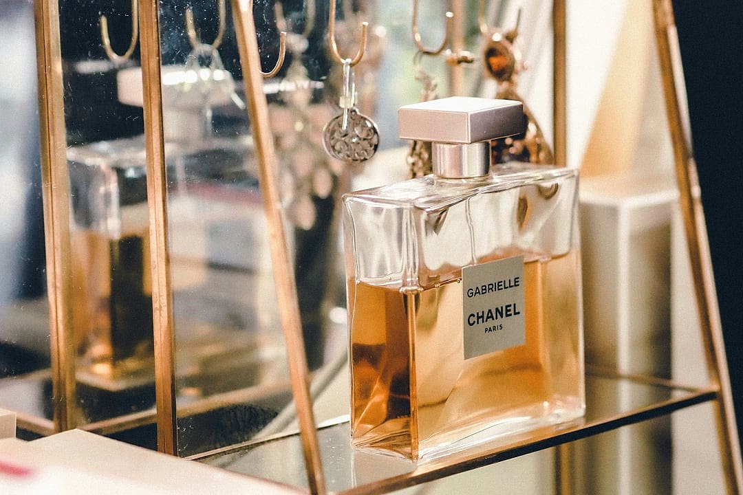 Chanel Gabrielle perfume bottle displayed in elegant glass case with gold accents, luxury fragrance presentation on mirrored shelf in Paris, France