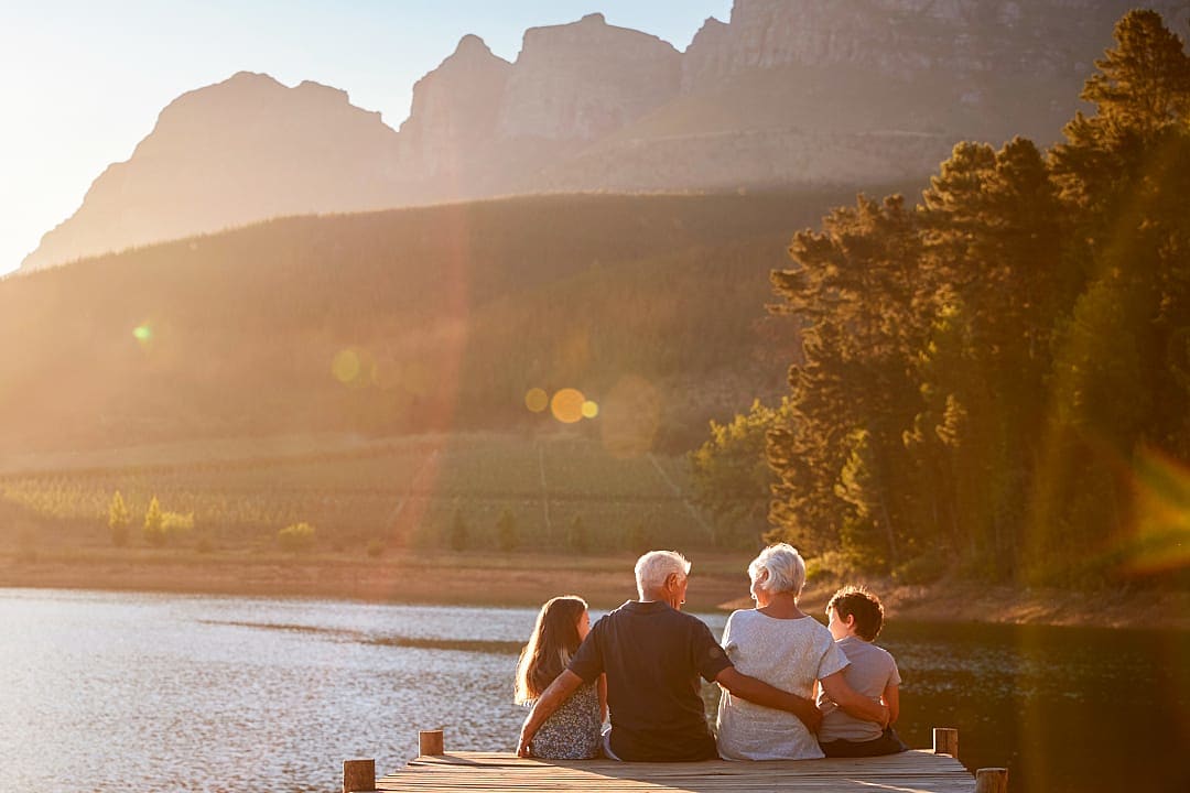 Grandchildren with grandparents sitting on a wooden jetty at a lake in Sommerset West near Cape Town, South Africa
