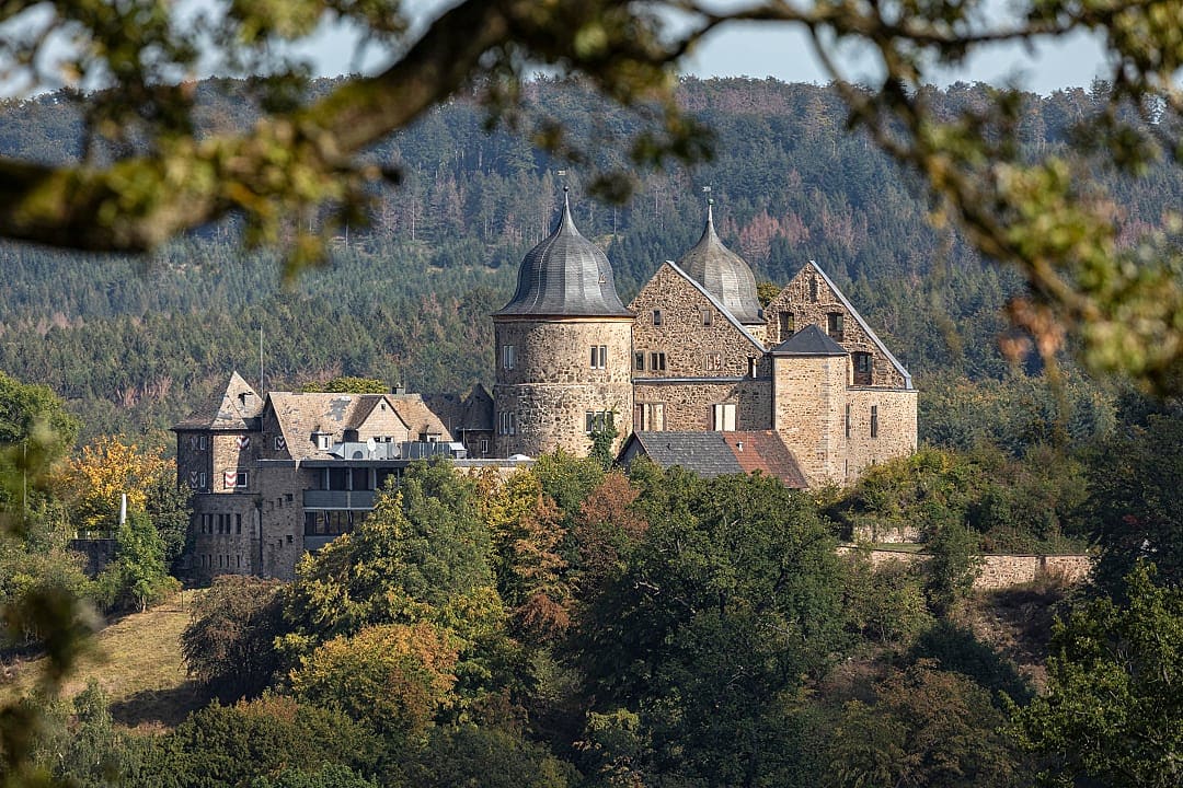 Sababurg Castle in Germany, the inspiration for the Brothers Grimm's Sleeping Beauty fairytale, surrounded by forested hills in autumn
