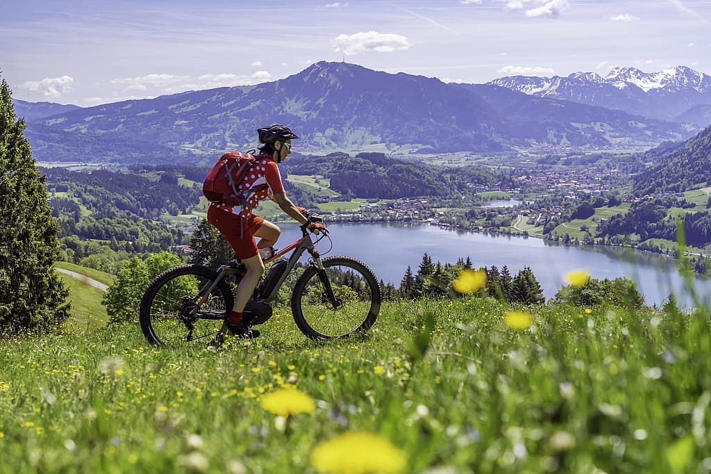 Woman mountain biking in Allgäu with a lake and mountains in the background
