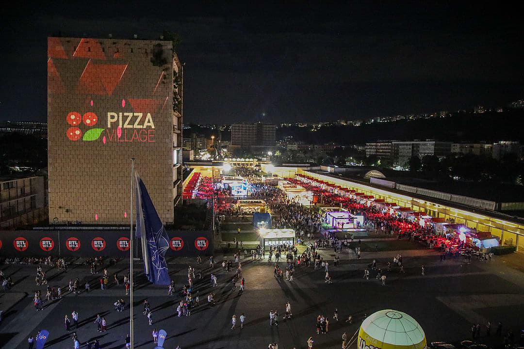 Night view of Napoli Pizza Village Festival, with crowds, food stalls, and illuminated signage in Naples