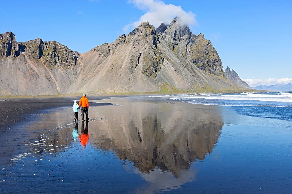 Father and son, walking on black sand at Stokksnes beach, enjoying scenery of Vestrahorn mountains in Iceland