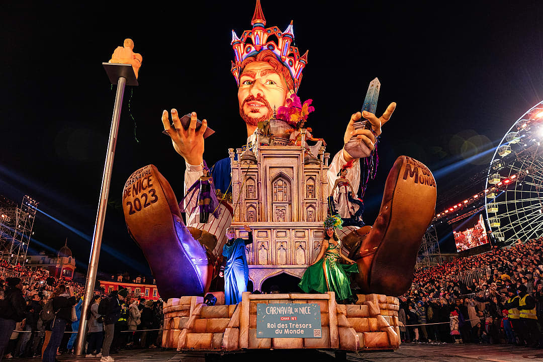 Colorful float with large, whimsical characters at the 2023 Nice Carnival in France, illuminated against a night sky with spectators enjoying the vibrant parade