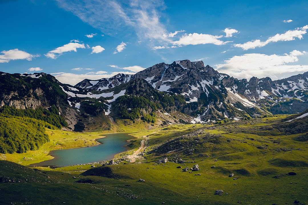Small blue glacial lake nestled between green hills and mountains.