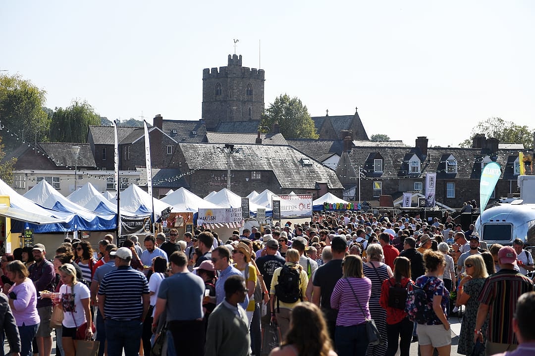 Crowds enjoying stalls and activities at Abergavenny Food Festival, with a historic tower in the background