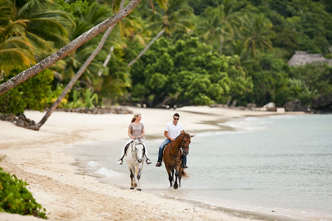 Couple horseback riding along the beach on Laucala Island.