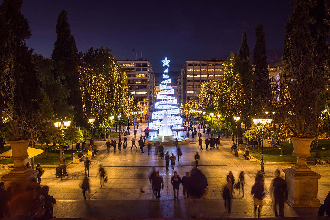 People walking under Christmas lights at Syntagma Square in Athens.