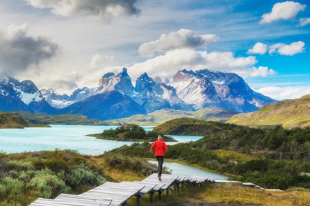 Hiker walks along boardwalk surrounded by Patagonian mountain scenery.