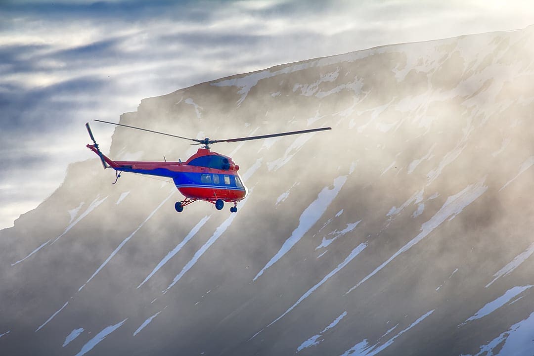 A helicopter hovers above snowy ridges in New Zealand’s Alps.
