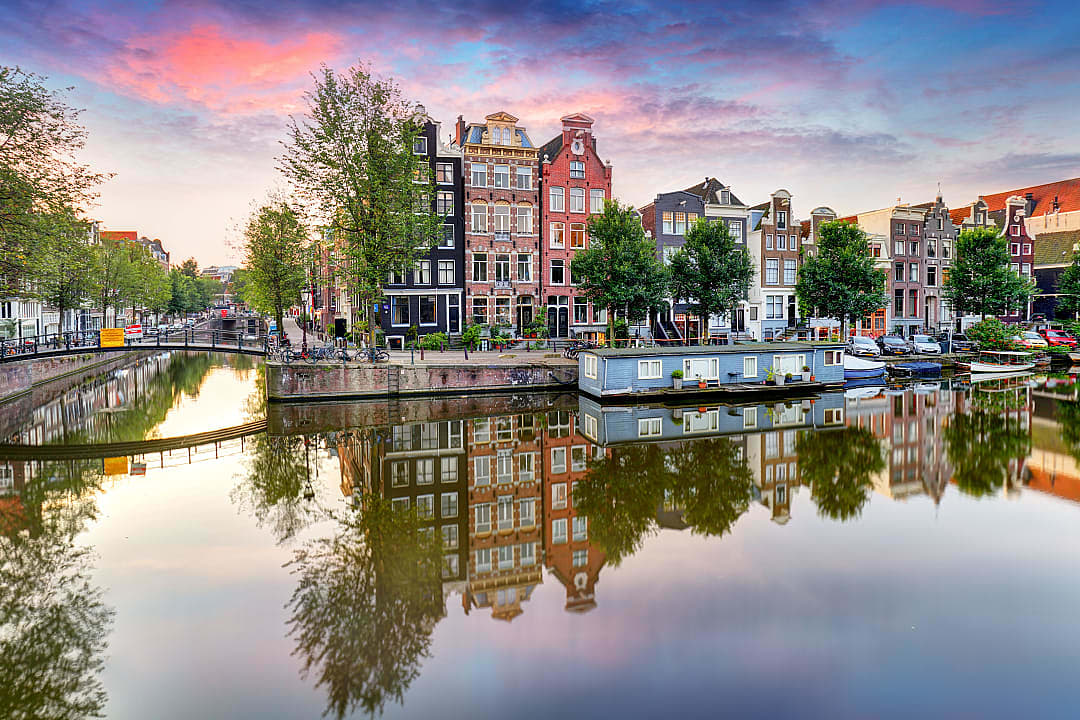 Scenic Amsterdam canal with traditional houses, houseboat, and vibrant sunset reflecting in the water