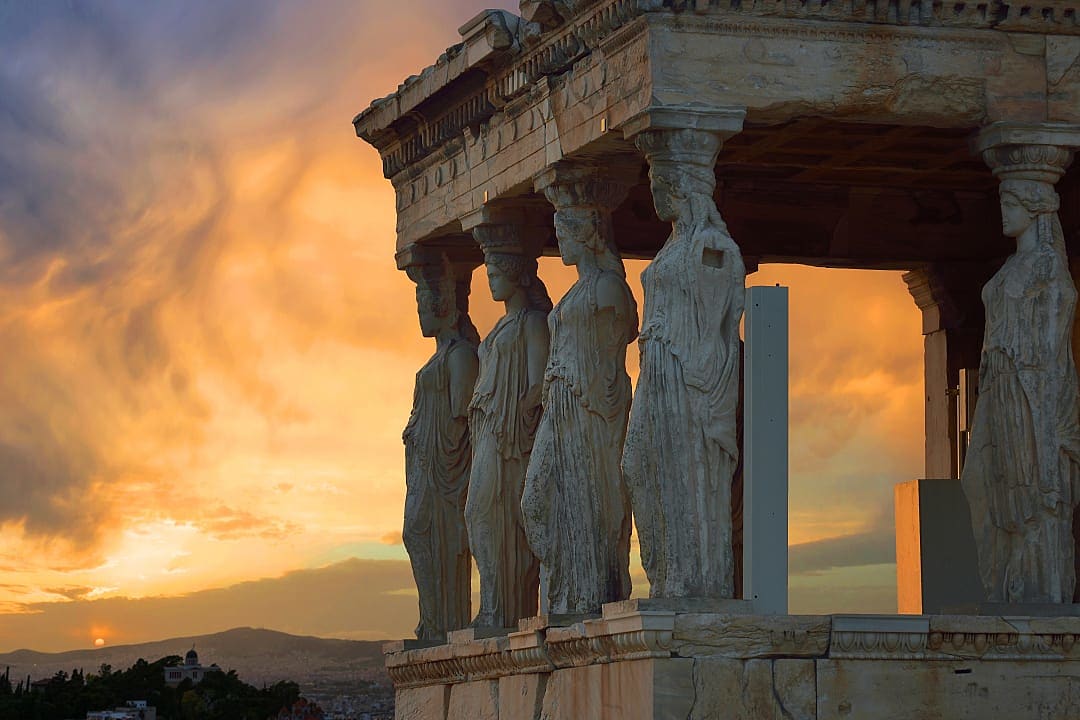 The Caryatids of the Erechtheion stand gracefully on Athens' Acropolis at sunset.