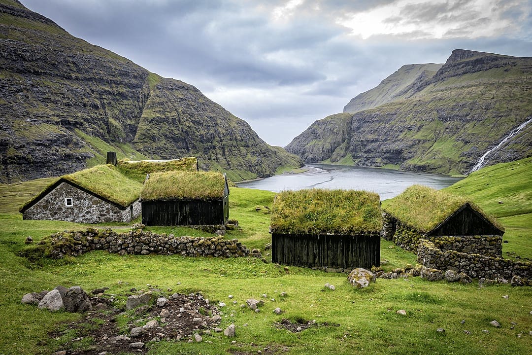 Turf-roof houses in the remote village of Saksun, Streymoy, Faroe Islands, with mountains and a tidal lagoon in the background.