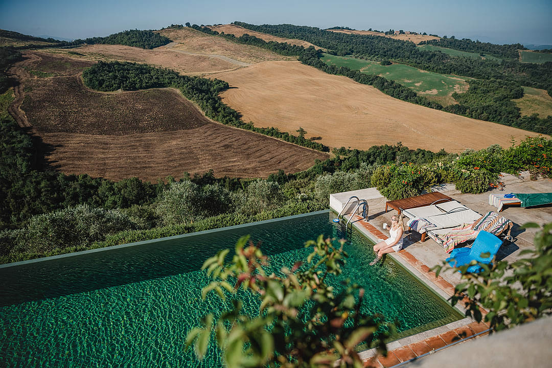 Woman Relaxing by a Pool Amidst the Patchwork Quilt of Silver-Green Tuscany Landscape.