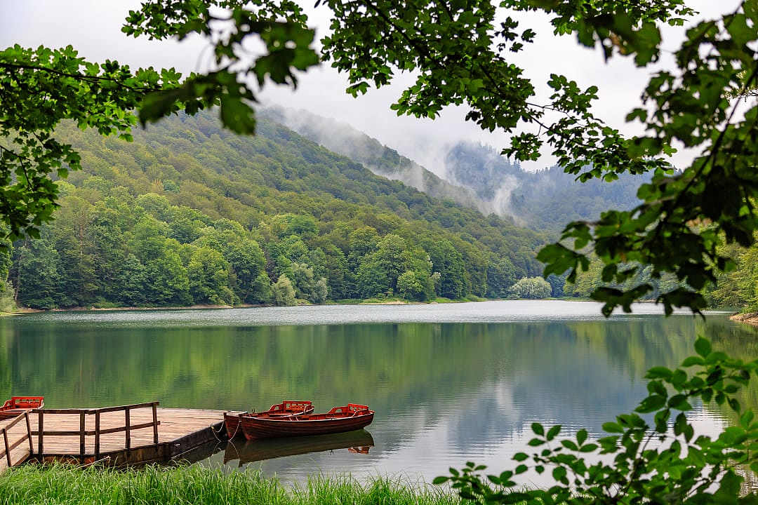 Small red boats docked on a calm lake surrounded by lush green mountains.