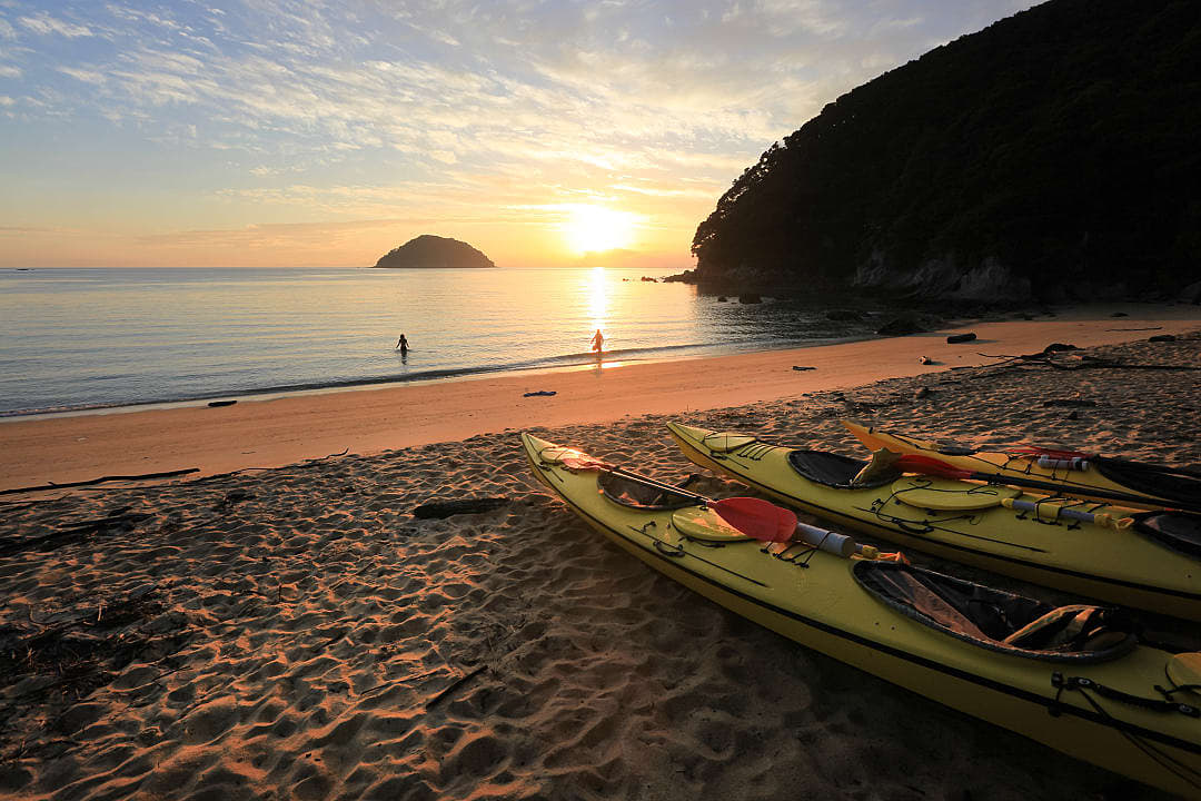 Three sea kayaks on a golden beach at sunrise in Tasman Abel National Park, New Zealand