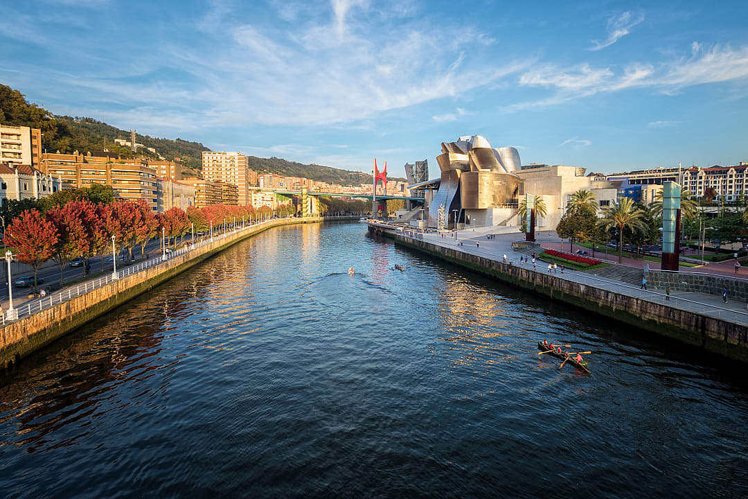 Rowers on the Nervión River beside the Guggenheim Museum in Bilbao, Spain, with cityscape and autumn trees