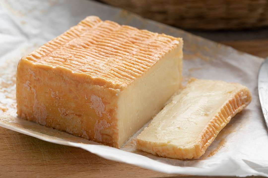 Close-up of a block of orange-rind Herve cheese with a sliced wedge.