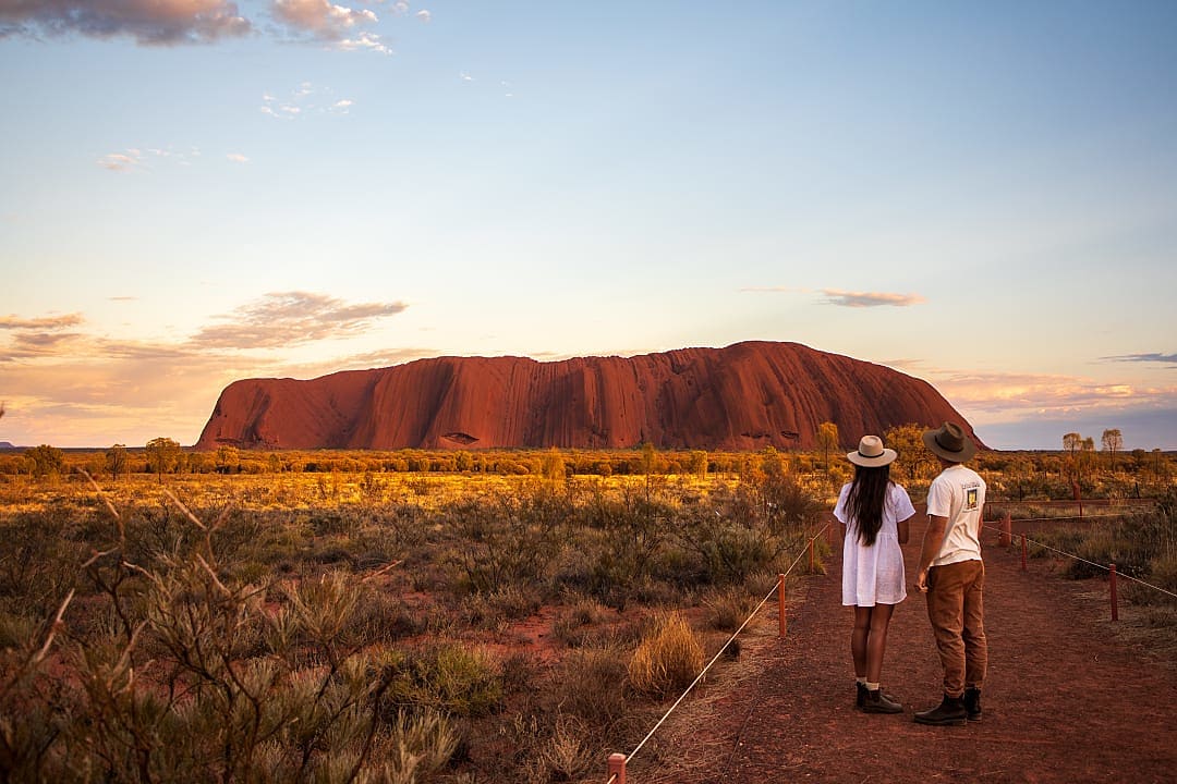 Couple admires Uluru’s golden sunset beauty.