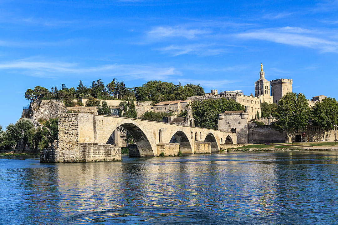 Pont Saint-Bénézet (Avignon Bridge) and the Palais des Papes (Pope's Palace) in Avignon, France, showcasing historic architecture and the Rhône River, under a clear blue sky.
