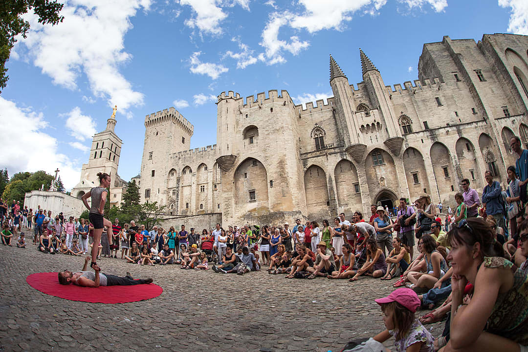 Street performance in front of the historic Palais des Papes in Avignon, France, drawing a lively crowd